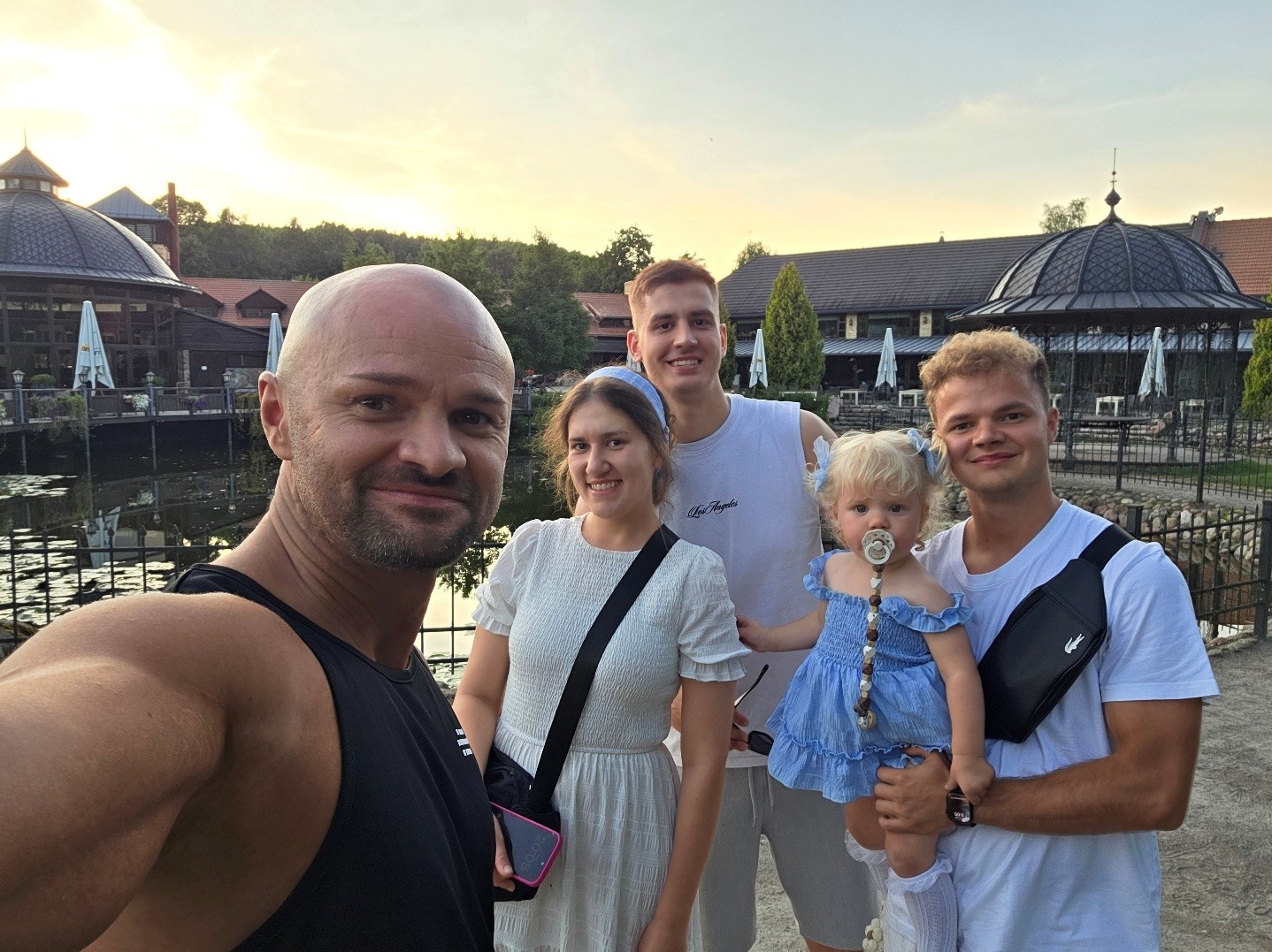Gruppenselfie von fünf Personen im Freien bei Sonnenuntergang an einem Teich.