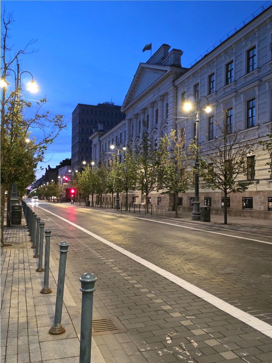 Straßenszene in der Dämmerung mit historischem Gebäude und beleuchteten Straßenlaternen.