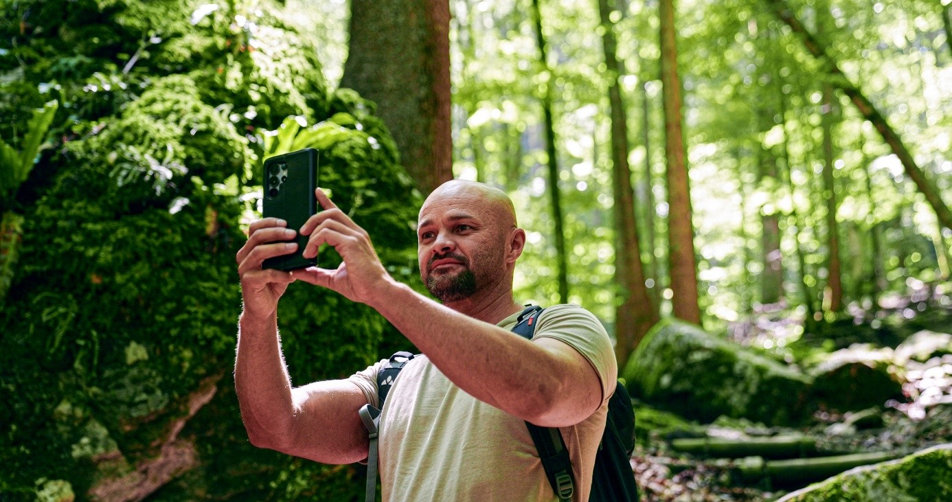 Eduard fotografiert mit dem Smartphone in einem üppig grünen Wald.
