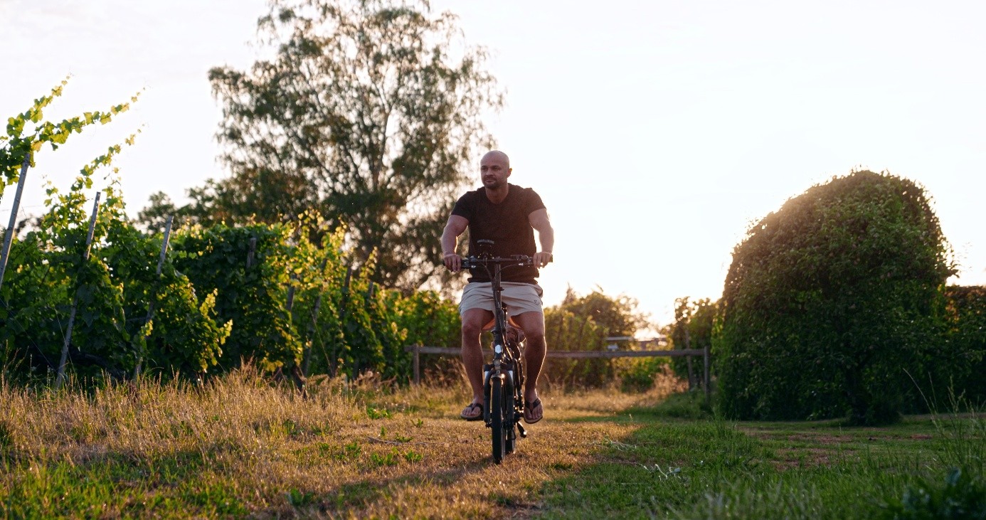 Eduard fährt bei Sonnenuntergang mit dem Rad über einen Feldweg neben Weinreben.