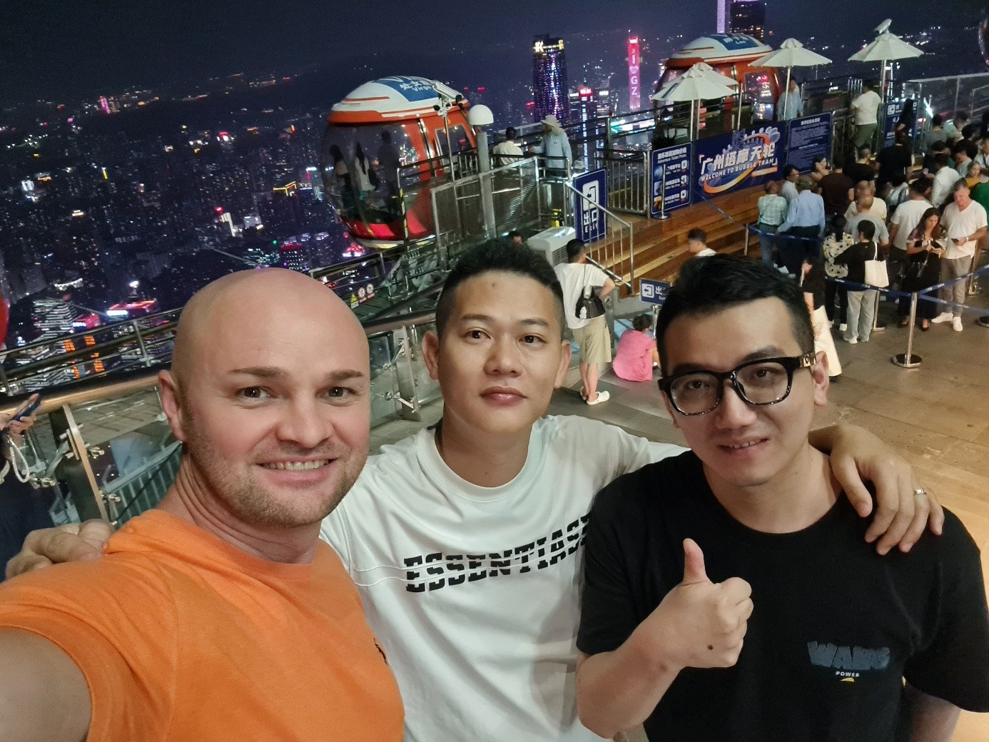 Drei Männer machen nachts ein Selfie auf einer Aussichtsplattform mit Skyline im Hintergrund.